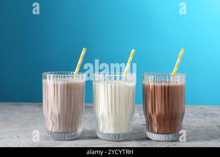 Köstliche Proteinshakes in Gläsern auf grauem, strukturiertem Tisch vor hellblauem Hintergrund Stockfoto