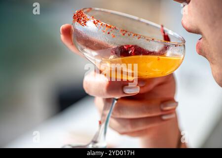 Ein lebhaftes Bild einer Frau, die eine scharfe Chili-Margarita genießt und den erfrischenden Geschmack und die farbenfrohe Präsentation des Cocktails in der Hand einfängt. Stockfoto