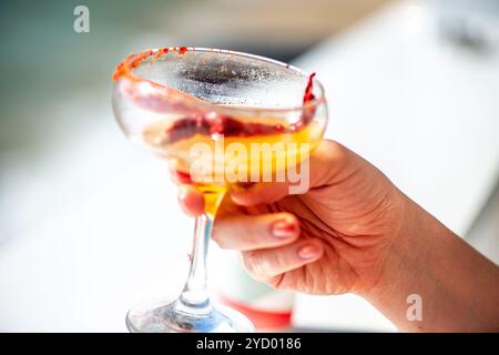 Ein lebhaftes Bild einer Frau, die eine scharfe Chili-Margarita genießt und den erfrischenden Geschmack und die farbenfrohe Präsentation des Cocktails in der Hand einfängt. Stockfoto