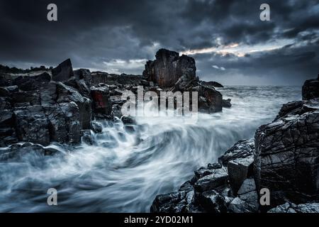 Der dramatische Himmel und die großen Wellen stürzen auf die Felsen der Küste Stockfoto