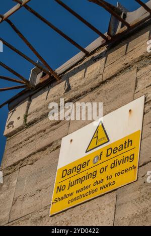 Gelbes Dreieck-Warnschild, das vor der Gefahr des Todes durch Springen oder Tauchen von den alten Mauern am Eingang zum Hafen von portsmouth, Großbritannien, warnt Stockfoto