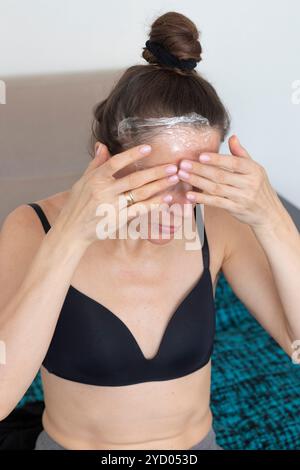 Frau, die ihr Gesicht und ihren Hals mit einer Frischhaltefolie als Hautpflegetherapie umwickelt Stockfoto