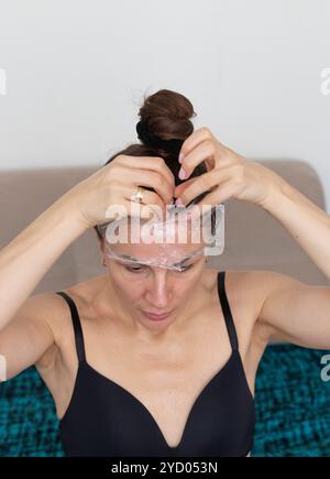 Frau, die ihr Gesicht und ihren Hals mit einer Frischhaltefolie als Hautpflegetherapie umwickelt Stockfoto