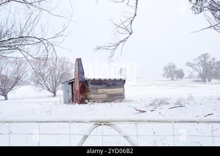 Baufällige rustikale Holzhütte mit Metallschornstein aus rostroten Patinen und gewelltem Eisendach, bedeckt mit einer Schneeschicht und gefrorenen Eiszapfen Stockfoto