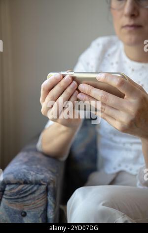 Eine Frau hält ein Smartphone mit beiden Händen horizontal, fokussiert auf den Bildschirm und sieht sich möglicherweise ein Video an. Stockfoto