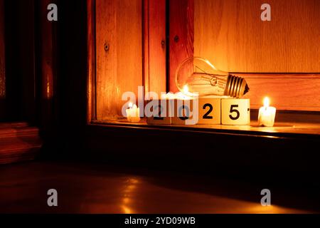 2025 auf Würfel geschrieben und eine Glühbirne zu Hause auf dem Boden mit Kerzen im Dunkeln, Silvester ohne Licht in der Ukraine Stockfoto