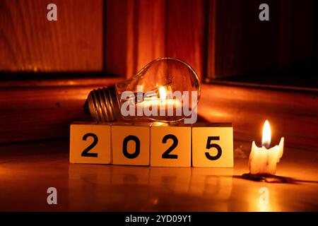 2025 auf Würfel geschrieben und eine Glühbirne zu Hause auf dem Boden mit Kerzen im Dunkeln, Silvester ohne Licht in der Ukraine Stockfoto