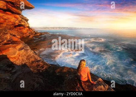 Weiblich auf Felsen, die das Meer um die Küstenfelsen kaskadieren Stockfoto