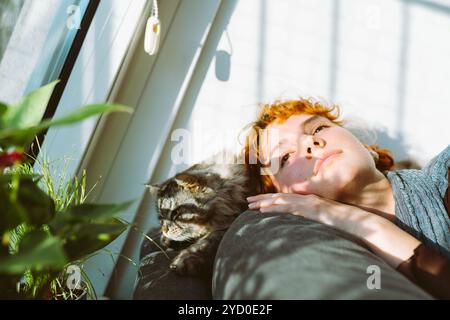 Porträt einer attraktiven jungen Frau und einer flauschigen Hauskatze nahe Fenster Stockfoto