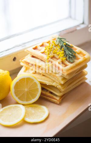 Wiener Waffeln stapeln sich und in Scheiben geschnittene Zitronen. Geschnittene Zitrone auf einem Holzbrett. Früchte werden gehackt. Saure Zitrone. Stockfoto