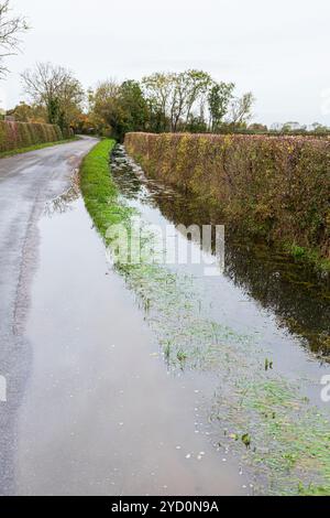 Ein Entwässerungsgraben, der nach starkem Regen in einer Straße in der Nähe des Dorfes Clanfield, Oxfordshire, England, überfließt Stockfoto