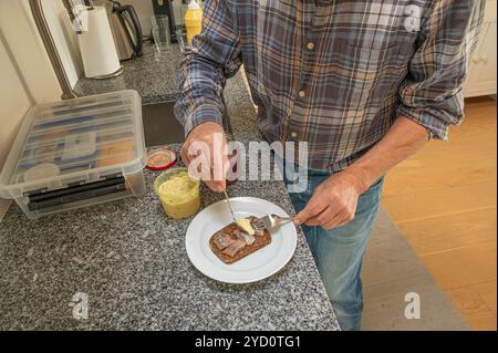 Ein Mann steht in der Küche und macht ein Sandwich mit Hering auf Roggenbrot, Dänemark, 24. Oktober 2024 Stockfoto