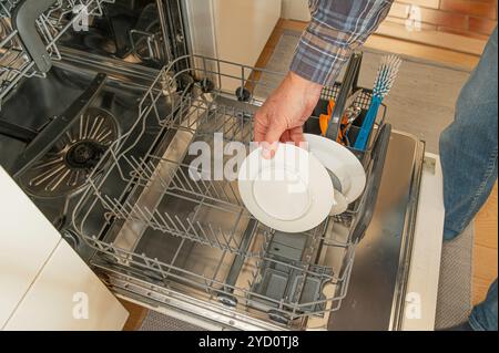 Ein Mann hält einen Teller in der Hand, den er in einen Geschirrspüler in der Küche legt, Dänemark, 24. Oktober 2024 Stockfoto