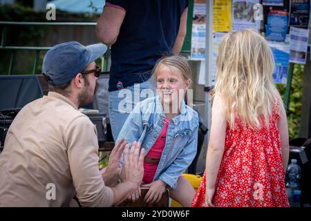 Lymm Food Festival 2024 – ein junges Mädchen in Jeansjacke sitzt auf einem Cajon und versucht, Musik zu machen, während ein Mann sie anweist Stockfoto