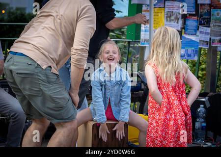 Lymm Food Festival 2024: Ein junges Mädchen in Jeansjacke sitzt auf einem Cajon und versucht Musik zu machen Stockfoto