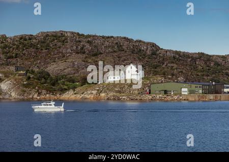 Ein Boot gleitet durch das klare Wasser einer Bucht, umgeben von zerklüfteten Klippen und bezaubernden Gebäuden in Bodo und zeigt Norwegens atemberaubende Küstenlandschaft Stockfoto