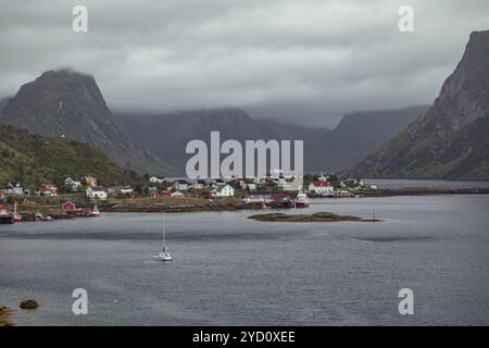 Reine, ein malerisches Dorf auf den Lofoten-Inseln, bietet traditionelle Häuser und Fischerboote inmitten atemberaubender Berglandschaften, umgeben von Wolken Stockfoto