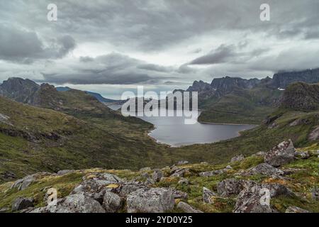 Eine atemberaubende Landschaft zeigt einen ruhigen See, umgeben von markanten Bergkämmen, mit dunklen Wolken über dem Himmel, die Wanderer einladen, die zu erkunden Stockfoto