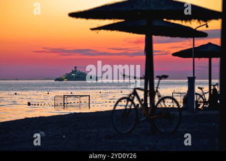 Strand und Sonnenschirme bei farbenfrohem Sonnenuntergang mit großem Blick auf die Jacht Stockfoto