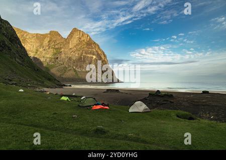 Erkunden Sie die atemberaubende Landschaft des Kvalvika Strandes, wo Camper einen ruhigen Abend inmitten majestätischer Klippen und lebhaftem Himmel in Lofoten, NOR genießen Stockfoto