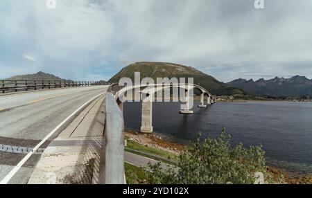 Die Bogenbrücke erstreckt sich über den See auf den Lofoten-Inseln und bietet einen atemberaubenden Blick auf die umliegenden Berge und die grüne Landschaft Stockfoto