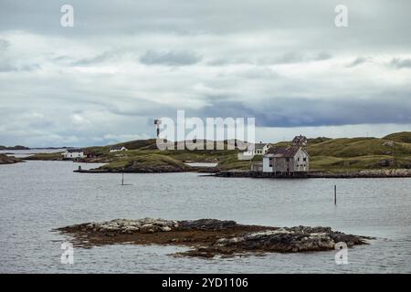 Die Lofoten-Inseln bieten ruhige Gewässer und traditionelle Küstengebäude, umgeben von üppigen Hochland und felsigen Küsten unter einem dramatischen Himmel. Stockfoto