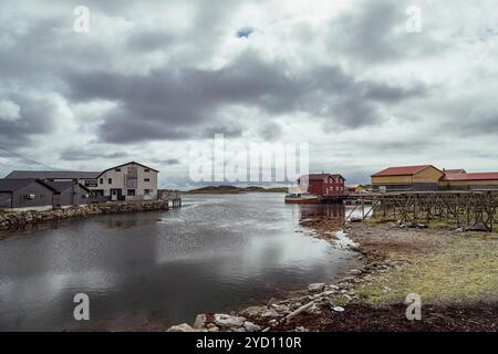 Diese beschauliche Winterlandschaft zeigt Holzhäuser entlang eines friedlichen Wasserkanals auf den Lofoten Inseln, die die ruhige nordische Atmosphäre widerspiegeln Stockfoto