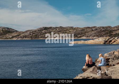 Bodo, Norwegen - 12. August 2018: Zwei junge Frauen sitzen auf einer Klippe mit Blick auf die wunderschöne Meeresbucht in Bodo, Lofoten Stockfoto