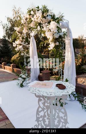 Eleganter Hochzeitsbogen mit Blumendesign und dekorativem Tisch im Außenbereich. Stockfoto