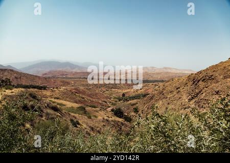 Die Sonne scheint hell über den weitläufigen Badlands in Marokko und hebt felsige Hänge und eine gewundene Feldstraße durch die zerklüftete Landschaft hervor. Chapar Stockfoto