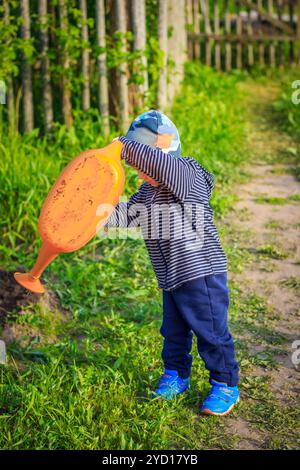 Ein kleiner Junge gießt Wasser aus der Gießkanne. Bewässerung der Betten. Gartenarbeit Stockfoto