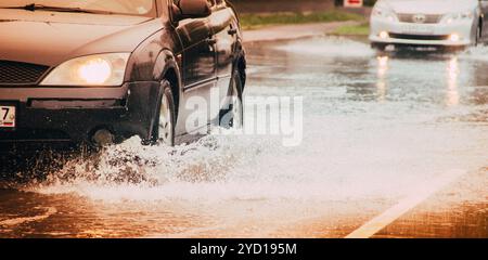 Das Auto fährt durch eine Pfütze. Pfützen auf der Straße. Wasser aus den Rädern. Straße nach dem Regen. . Russland, Region Leningrad, GATC Stockfoto