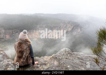 Frau, die auf einem Felsvorsprung sitzt und in den Nebel blickt Stockfoto