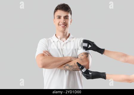 Tätowiermeister hält Creme mit Spray und Mann auf hellem Hintergrund Stockfoto
