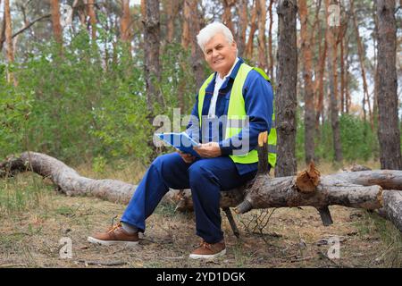 Leitender Forstwirt mit Klemmbrett, der auf Baumstämmen im Wald sitzt Stockfoto