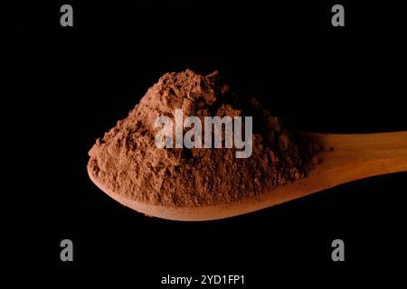 Hoher Winkel von Holzlöffel mit Kakaopulver auf schwarzem Hintergrund Stockfoto