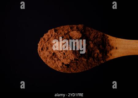 Zenithal-Schuss von Holzlöffel mit Kakaopulver auf schwarzem Hintergrund Stockfoto