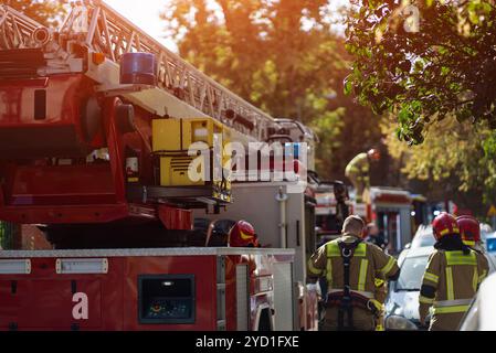 Feuerwehrleute reagieren auf Notfälle, Feuerwehrfahrzeuge mit Leitern und blinkenden blauen Lichtern. Feuerwehrleute in Ausrüstung bereiten Ausrüstung in Wohngebieten vor Stockfoto