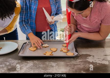 Weihnachtskekse dekorieren, multirassische weibliche Freunde, die festliche Feiertagsaktivitäten teilen, zu Hause Stockfoto