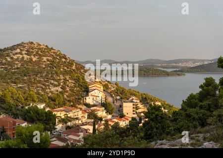Charmantes Küstendorf auf einem sonnengeküssten Hügel mit Blick auf das ruhige Meer und die nahe gelegenen Inseln in der Abenddämmerung. Stockfoto