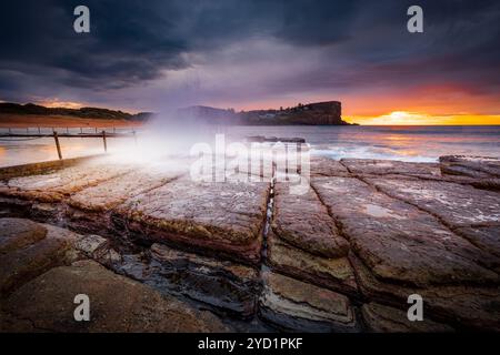 Sonnenaufgangshimmel und Wellen krachen am felsigen Strand Stockfoto