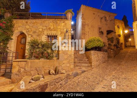 Nachtansicht auf die enge Kopfsteinpflasterstraße mit traditionellen Steinhäusern und Statue, die von Straßenlaternen beleuchtet wird, in Tossa de Mar, Girona, Spanien, Stockfoto