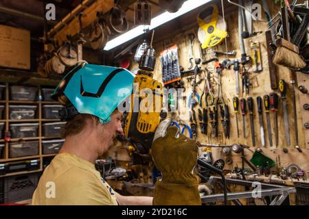 Eine Detailansicht der Schmied Holding eine elektrische Bohrmaschine in seiner Werkstatt. Qualifizierte Handwerker Tragen von Schutzausrüstungen und die Verwendung von Power Tools. Stockfoto