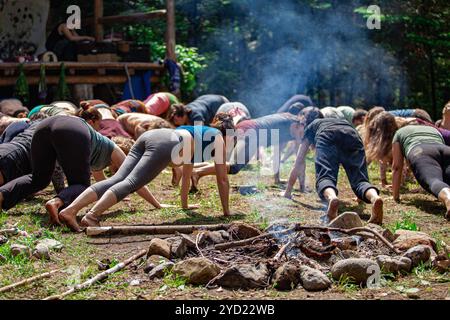 Eine große Gruppe von Personen zwischen den Generationen werden gesehen Üben eingedenk Yoga in der Nähe von einem Lagerfeuer stellt an einem Wochenende mit multikulturellen Erfahrungen. Stockfoto