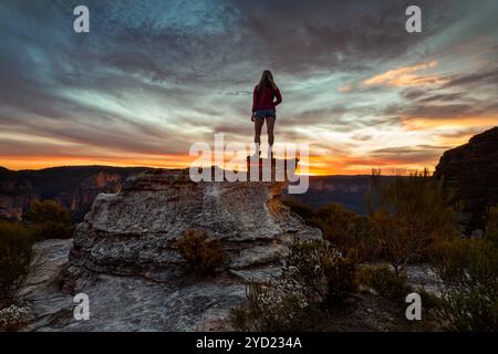 Weibliche Wanderer stehen auf einem Felsvorsprung auf dem Berggipfel entlang der Klippen der Blue Mountains und genießen spektakuläre Ausblicke bei Sonnenuntergang. Stockfoto