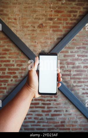 Eine Hand hält ein leeres Smartphone an einer Ziegelwand und bietet eine moderne Kulisse für Branding Stockfoto