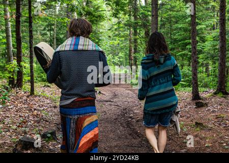 Ein junges Paar gesehen werden entlang einer Spur im dichten Wald, der Kerl trägt einen heiligen Native drum während einer multikulturellen Festival in natürlichen surro Stockfoto