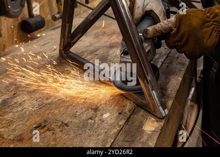 Eine Detailansicht von heißen Funken fliegen von der Schleifscheibe mit einem Winkelschleifer, während ein Schmied Polituren einen Metallrahmen. Stockfoto