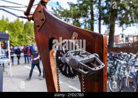 Eine Nahaufnahme der Details eines Holzfahrrads stand am Ende Metallkette und -Pedal sind im Vordergrund, geparkte Fahrräder und verschwommene Menschen im Hintergrund zu sehen Stockfoto