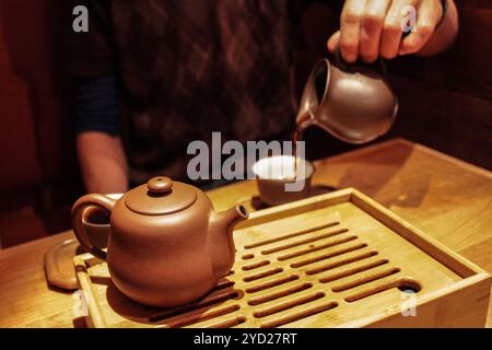 Gießen Sie dunklen pu-erh-Tee aus einem violetten Tongefäß in eine kleine Verkostungstasse Stockfoto